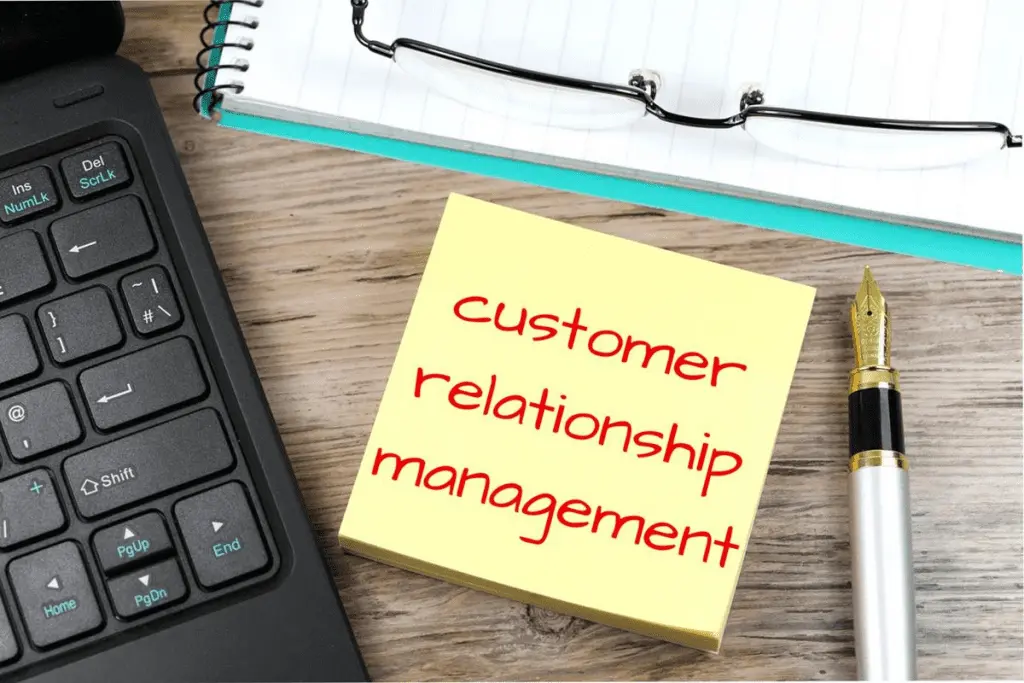 A sticky note reading 'customer relationship management' beside a laptop keyboard and pen