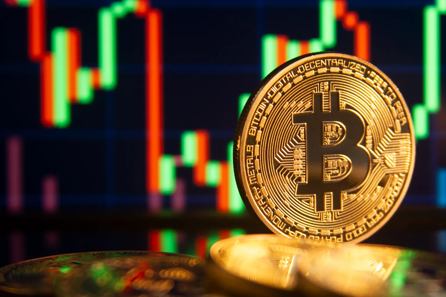 A gold Bitcoin coin in front of a blurred candlestick trading chart
