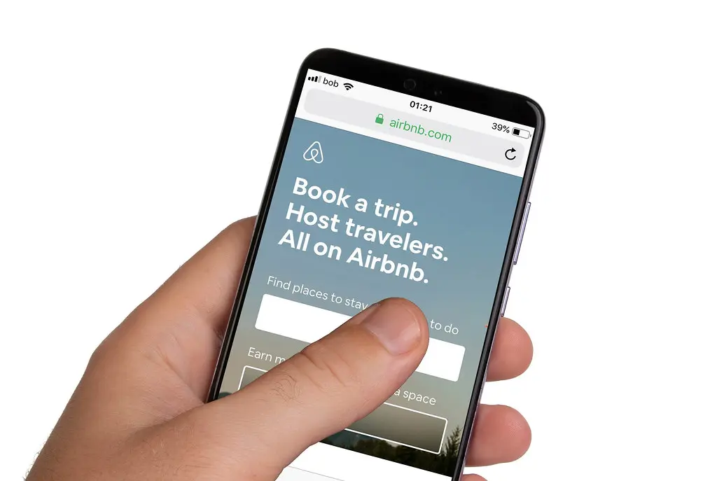 A hand holding a phone showing Airbnb's mobile site, an example of an on-demand app